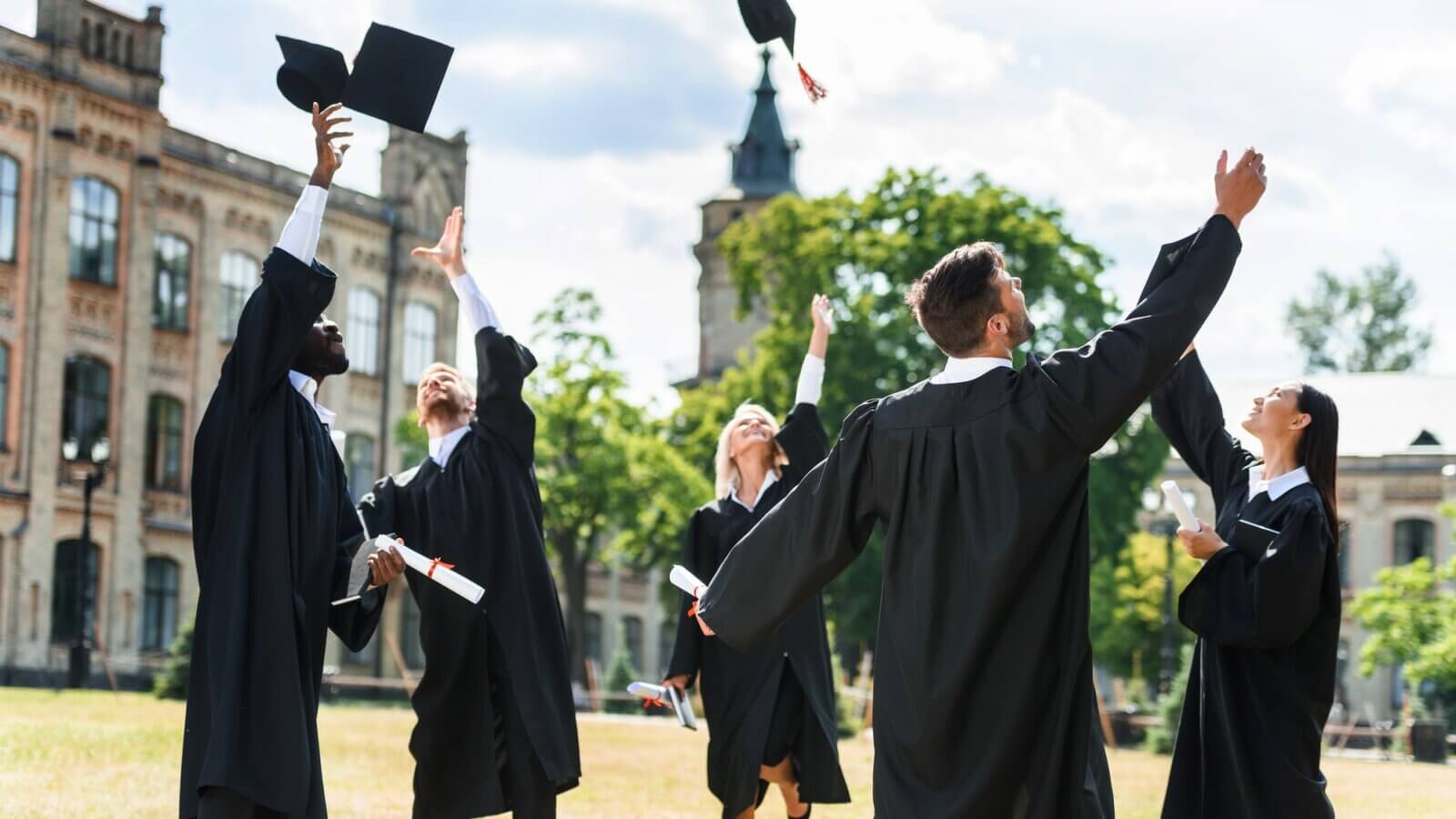 young graduated students throwing up graduation caps in university garden