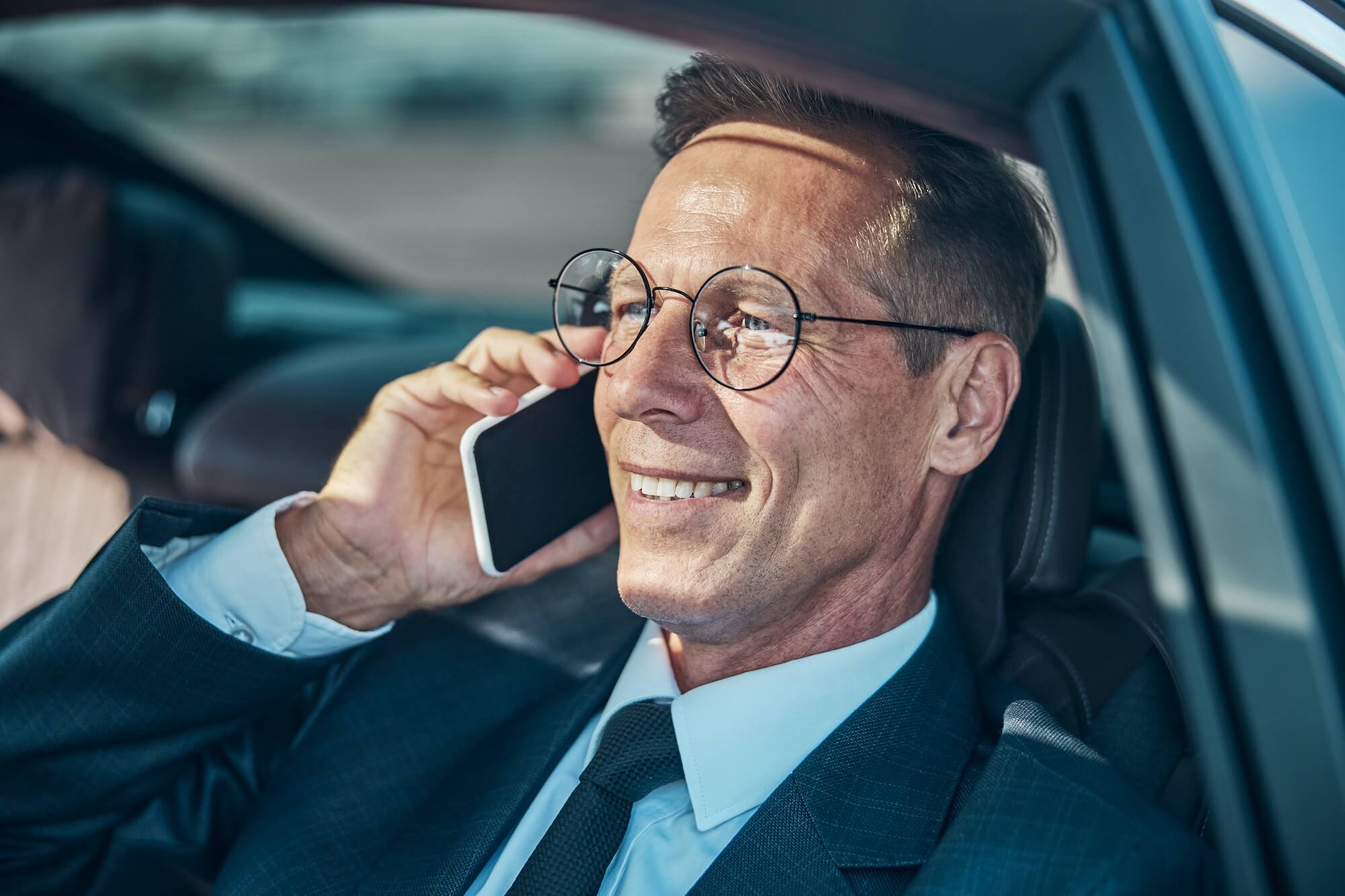 Happy mature man talking on smartphone in car