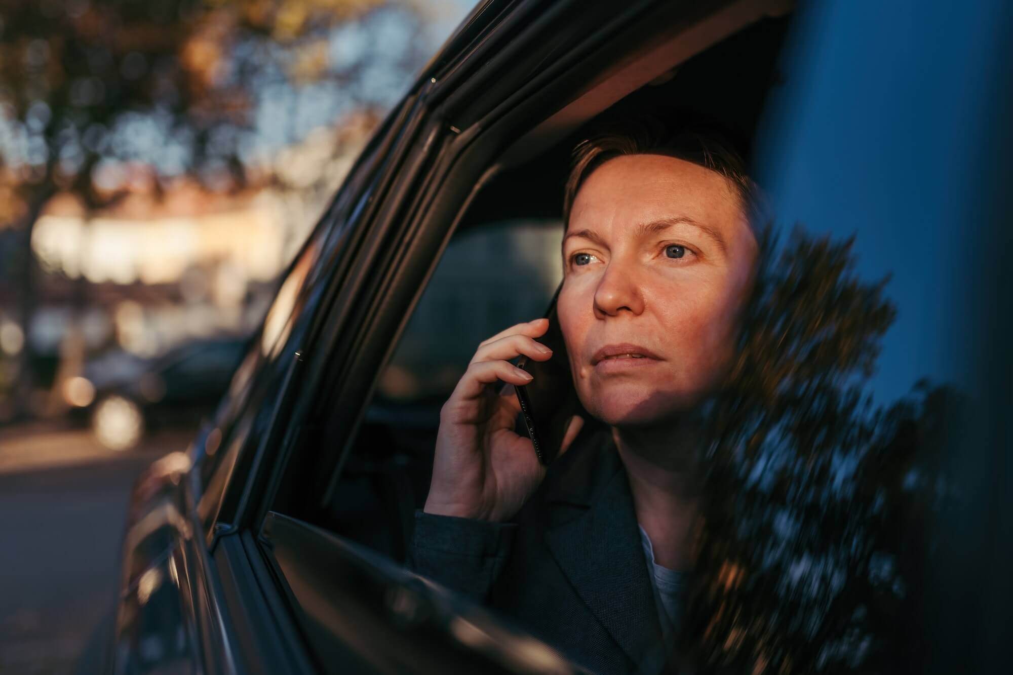 Serious businesswoman talking on mobile phone from the backseat of the car