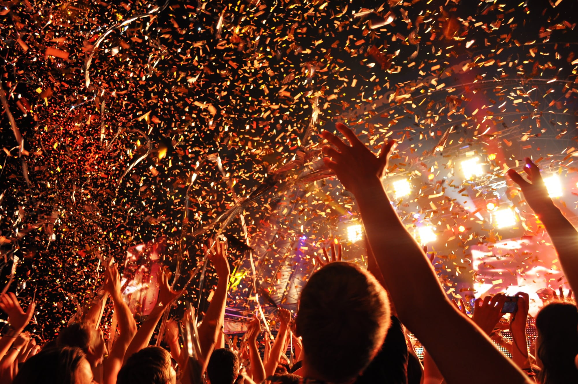 Happy crowd of people at the music concert raise their hands up with a decor and serpentine