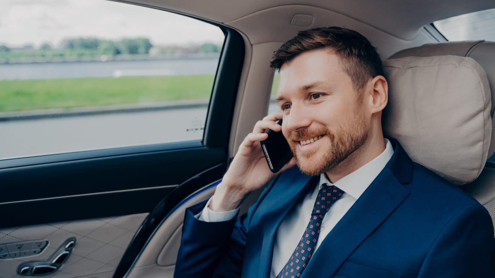 Attractive skilled banker in formal suit riding in corporate car and talking on cellphone