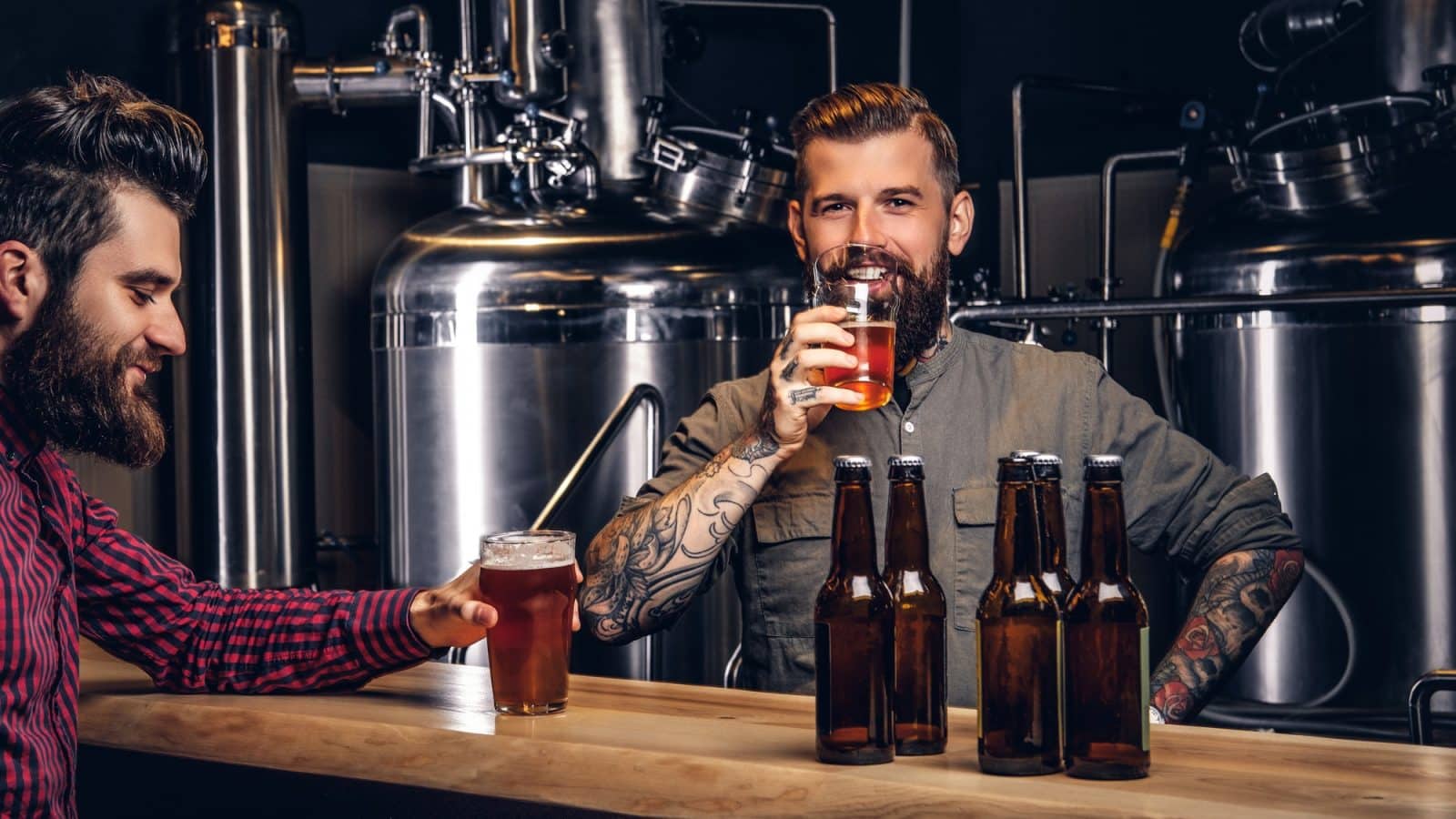 Two stylish bearded hipsters friends drinking craft beer together at the indie brewery.